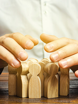Des mains au dessus d'un groupe de personnages en bois en signe de protection - MACSF