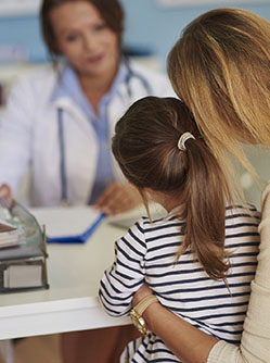 Une femme médecin à son bureau face à sa jeune patiente accompagnée de sa maman - MACSF