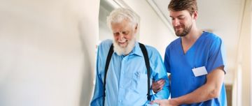 Un aide-soignant tient le bras d'un homme âgé pour l'aider à marcher dans le couloir de l'hôpital - MACSF