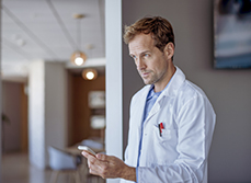Un homme médecin tient un téléphone à son domicile - MACSF