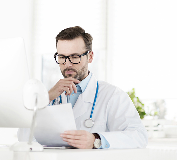 Une médecin en blouse blanche lit attentivement un document à son bureau - MACSF