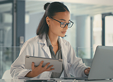 Une femme médecin face à son ordinateur tenant à la main une tablette - MACSF