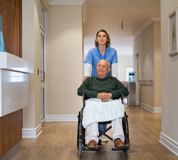 Aide-soignante qui aide un patient dans son fauteuil roulant