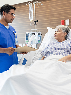 Une patiente dans son lit d'hopital discute avec un soignant tenant un dossier médical - MACSF