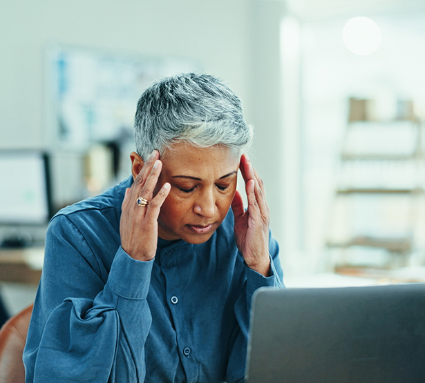 Une femme d'une cinquantaine d'années se tient les tempes devant sont pc portable - MACSF