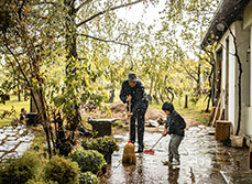 Un père et son enfant balayent une terrasse après une grosse pluie - MACSF