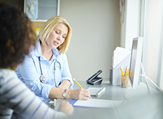 Une médecin assise à son bureau, en compagnie d'une patiente, rédige un document - MACSF