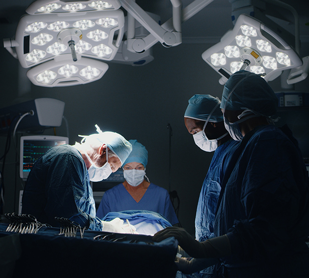 Equipe médicale exécutant une chirurgie, éclairée par les projecteurs d'une salle d'opération sombre - MACSF