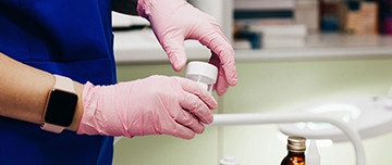 Gros plan sur les mains gantées d'une technicienne de laboratoire tenant un flacon de prélèvement - MACSF
