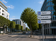 Un milieu urbain dans lequel se trouve un panneau de signalisation qui pointe vers des établissements de santé - MACSF