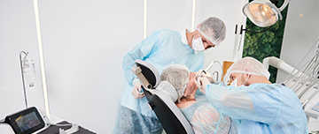 Une patiente sur le fauteuil du dentiste entourée de deux praticiens - MACSF