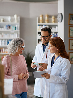 Deux pharmaciens souriants conseillent une cliente âgée - MACSF