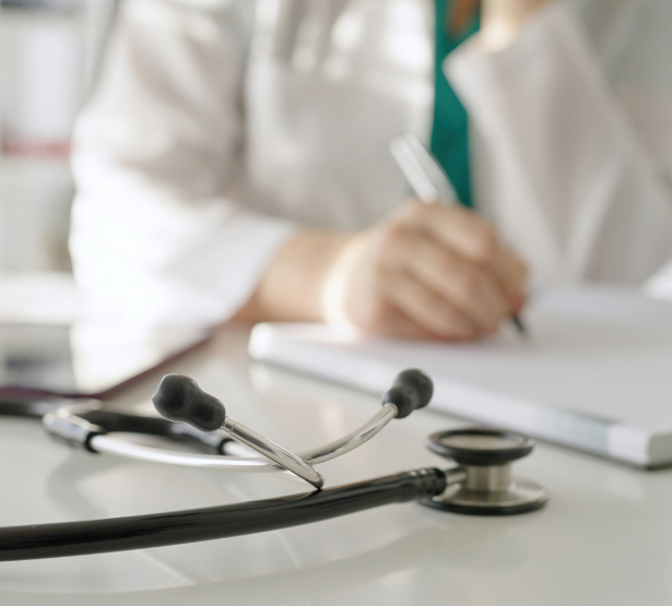 Un stéthoscope posé sur un bureau avec une professionnelle de santé qui prend des notes en arrière-plan - MACSF