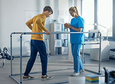 Un jeune homme marche en se tenant à des barres face à une kinésithérapeute - MACSF