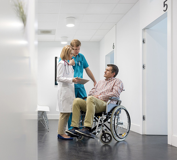 Un homme en fauteuil roulant discute avec l'infirmière dans le couloir de l'hôpital - MACSF