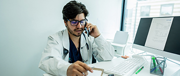 Médecin assis à son bureau et parlant au téléphone - MACSF