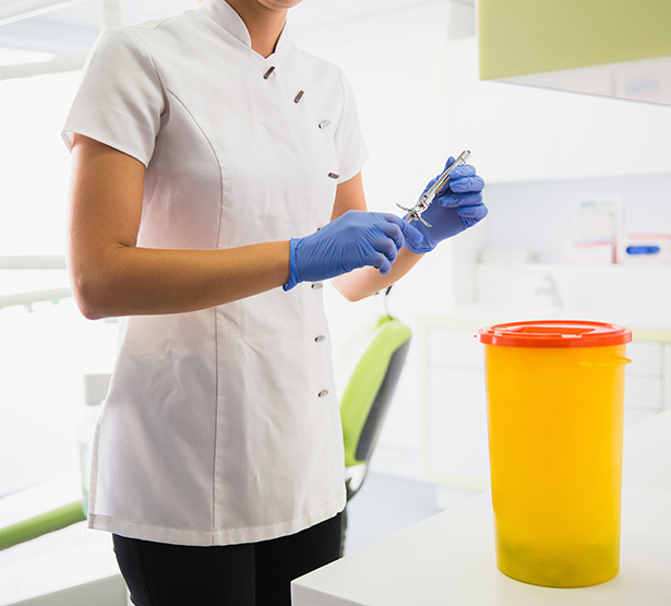 Une technicienne de cabinet dentaire s'apprête à mettre une seringue dans un bac à déchets médicaux - MACSF