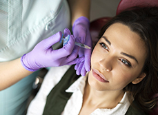 Main gantées procédant à une injection d'acide hyaluronique sur les pommettes d'une patiente - MACSF