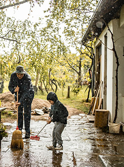Un père et son enfant balayent une terrasse après une grosse pluie - MACSF