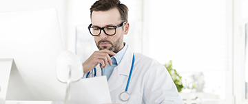 Une médecin en blouse blanche lit attentivement un document à son bureau - MACSF