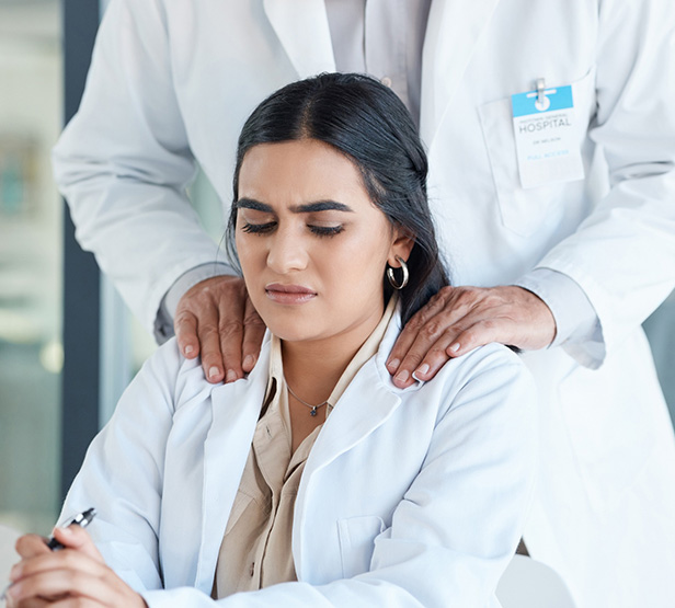 Soignante à son bureau, mal à l’aise, tandis qu’un collègue lui pose les mains sur les épaules - MACSF