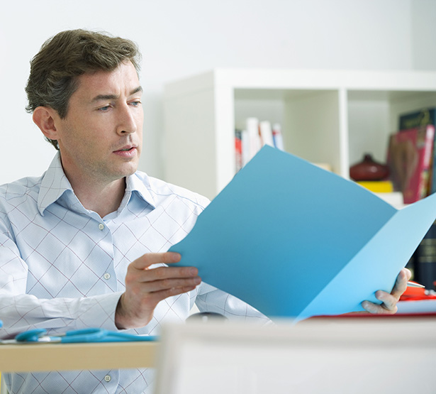 Un médecin, assis à son bureau, consulte un dossier médical - MACSF