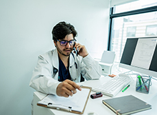 Médecin assis à son bureau et parlant au téléphone - MACSF