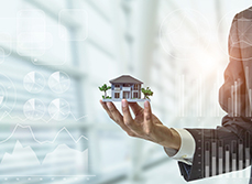 Une main tenant une maquette de maison avec des statistiques en filigrane - MACSF