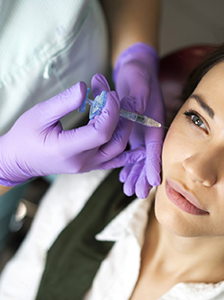 Main gantées procédant à une injection d'acide hyaluronique sur les pommettes d'une patiente - MACSF