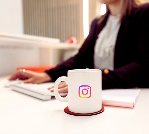 Gros plan sur un mug décoré sur logo instagram et en arrière plan le buste d'une femme qui a les mains posées sur son clavier - MACSF