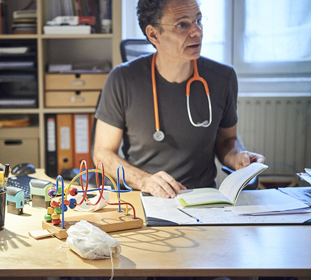 Un pédiatre assis à son bureau consulte le carnet de santé - MACSF