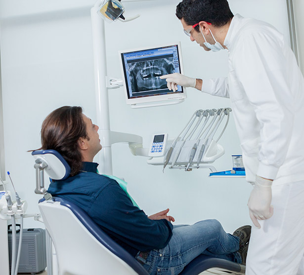 Le dentiste pointe une radio dentaire en expliquant les soins au patient - MACSF
