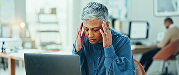 Une femme d'une cinquantaine d'années se tient les tempes devant sont pc portable - MACSF