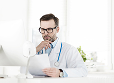 Une médecin en blouse blanche lit attentivement un document à son bureau - MACSF