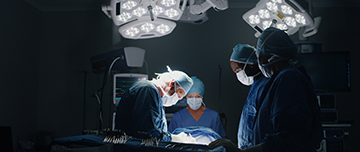 Equipe médicale exécutant une chirurgie, éclairée par les projecteurs d'une salle d'opération sombre - MACSF