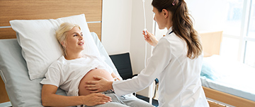 Une sage-femme examine une patiente enceinte allongée dans un lit d’hôpital  - MACSF