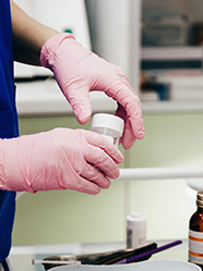 Gros plan sur les mains gantées d'une technicienne de laboratoire tenant un flacon de prélèvement - MACSF