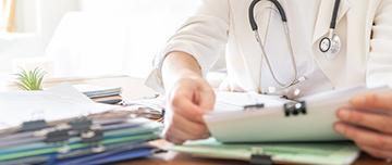 Un médecin examine une pile de dossiers de patients - MACSF