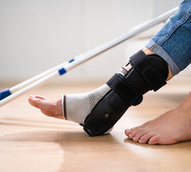 Une personne porte une attelle de cheville, avec des béquilles visibles en arrière-plan - MACSF