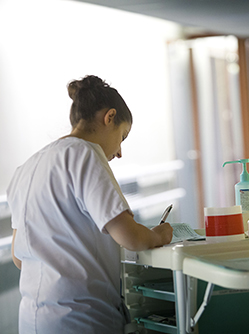 Une infirmière dans un couloir note les soins effectués - MACSF