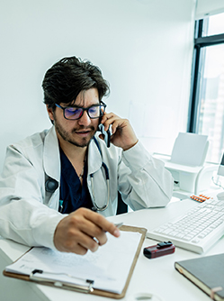 Médecin assis à son bureau et parlant au téléphone - MACSF