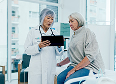 Deux femmes d'âge mûr, patiente et médecin, contrôlent des résultats médicaux sur une tablette - MACSF