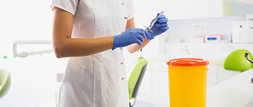 Une technicienne de cabinet dentaire s'apprête à mettre une seringue dans un bac à déchets médicaux - MACSF