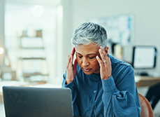 Une femme d'une cinquantaine d'années se tient les tempes devant sont pc portable - MACSF