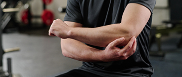 Un homme assis dans la salle du kinésithérapeute se tient le coude - MACSF