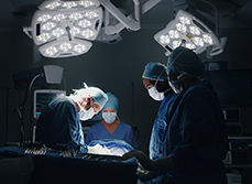 Equipe médicale exécutant une chirurgie, éclairée par les projecteurs d'une salle d'opération sombre - MACSF