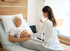 Une sage-femme examine une patiente enceinte allongée dans un lit d’hôpital  - MACSF