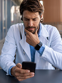 Un professionnel de santé regarde son smartphone d'un air soucieux - MACSF