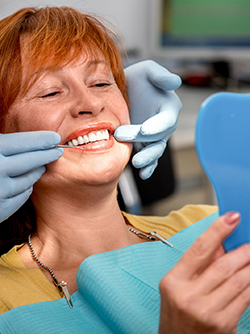Tenant un miroir, la patiente regarde ses prothèses dentaires - MACSF
