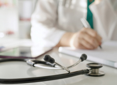 Un stéthoscope posé sur un bureau avec une professionnelle de santé qui prend des notes en arrière-plan - MACSF
